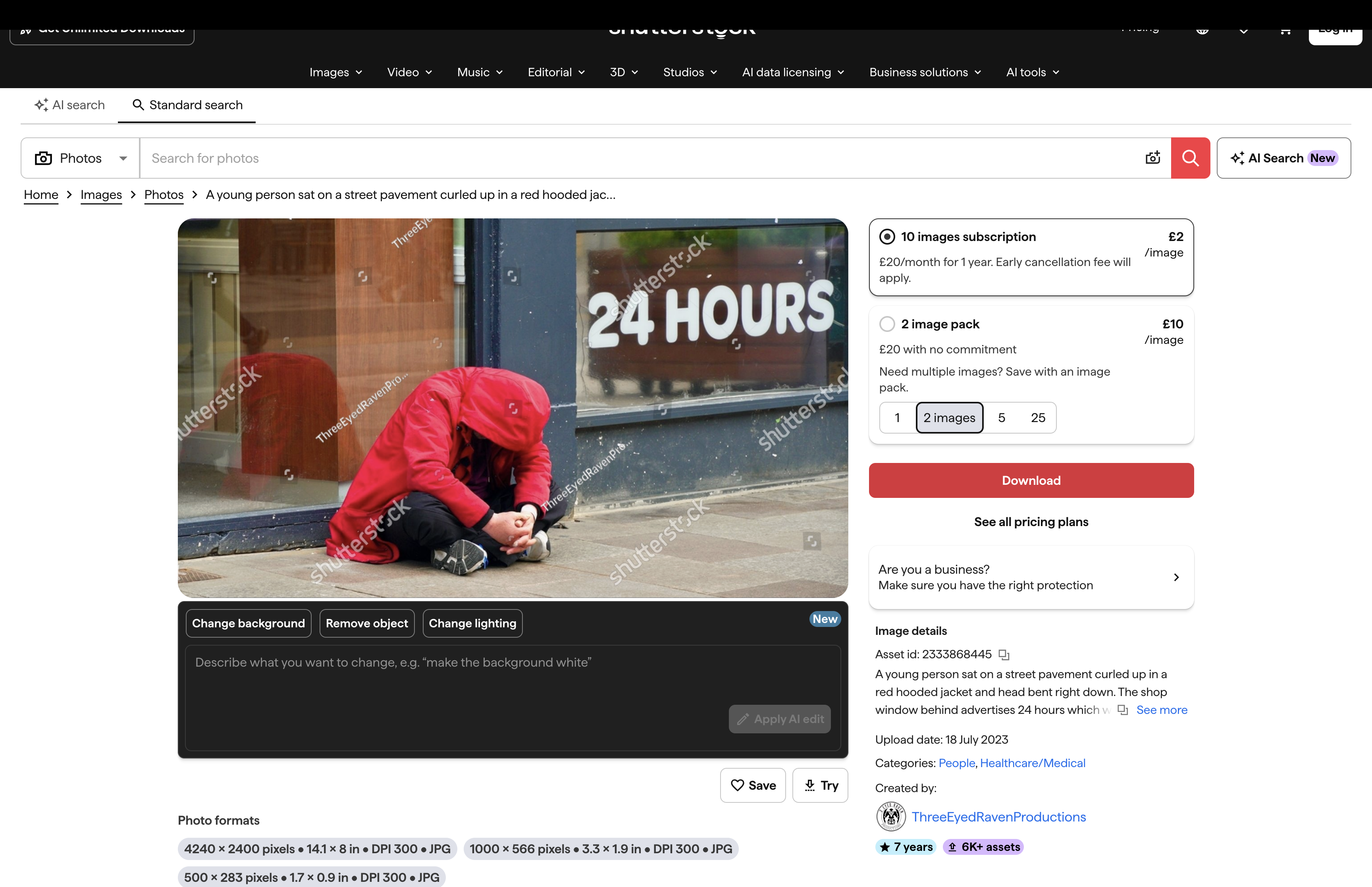 Person in a bright red coat sitting on a pavement outside a shop.
